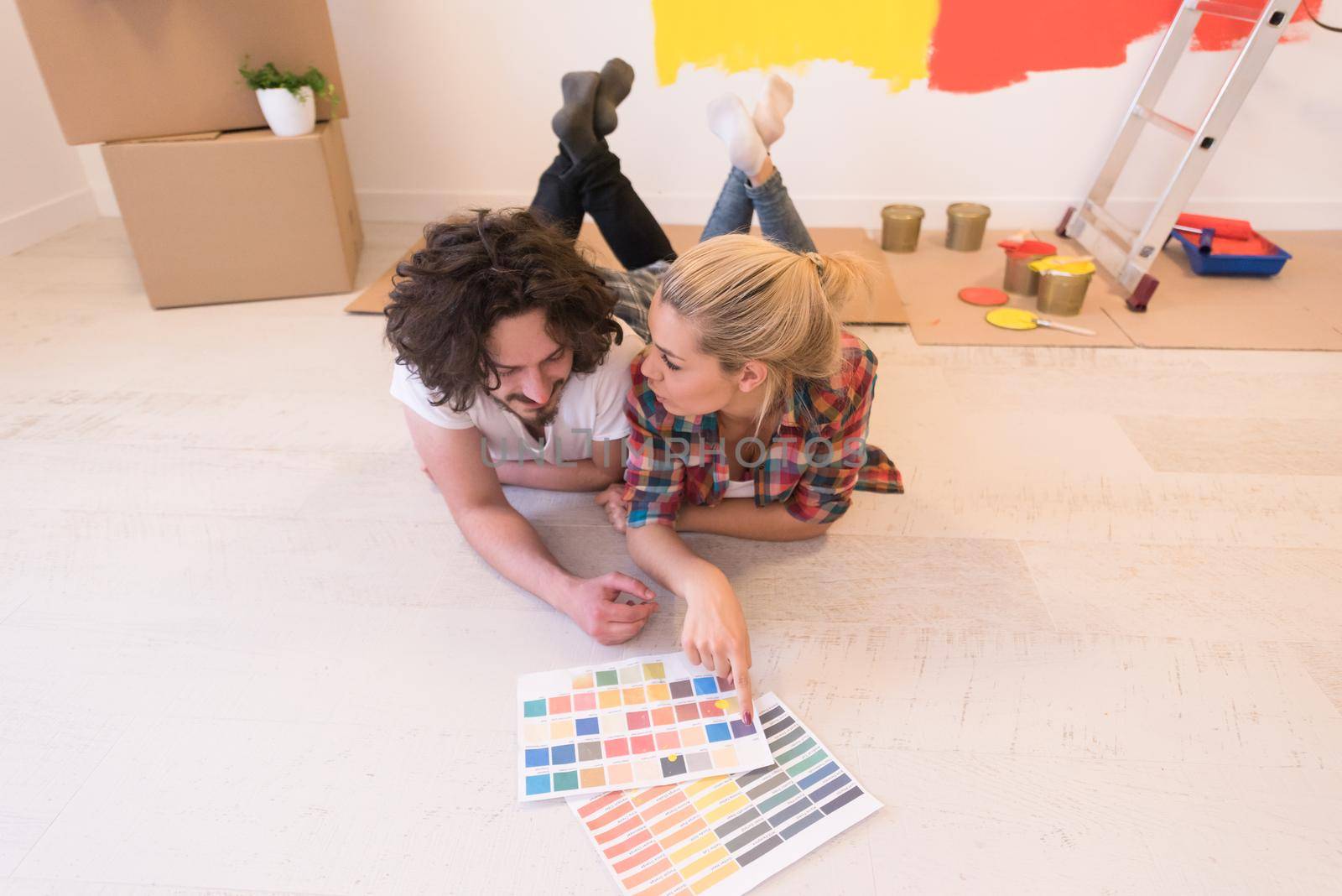 Happy young couple relaxing after painting a room in their new house on the floor