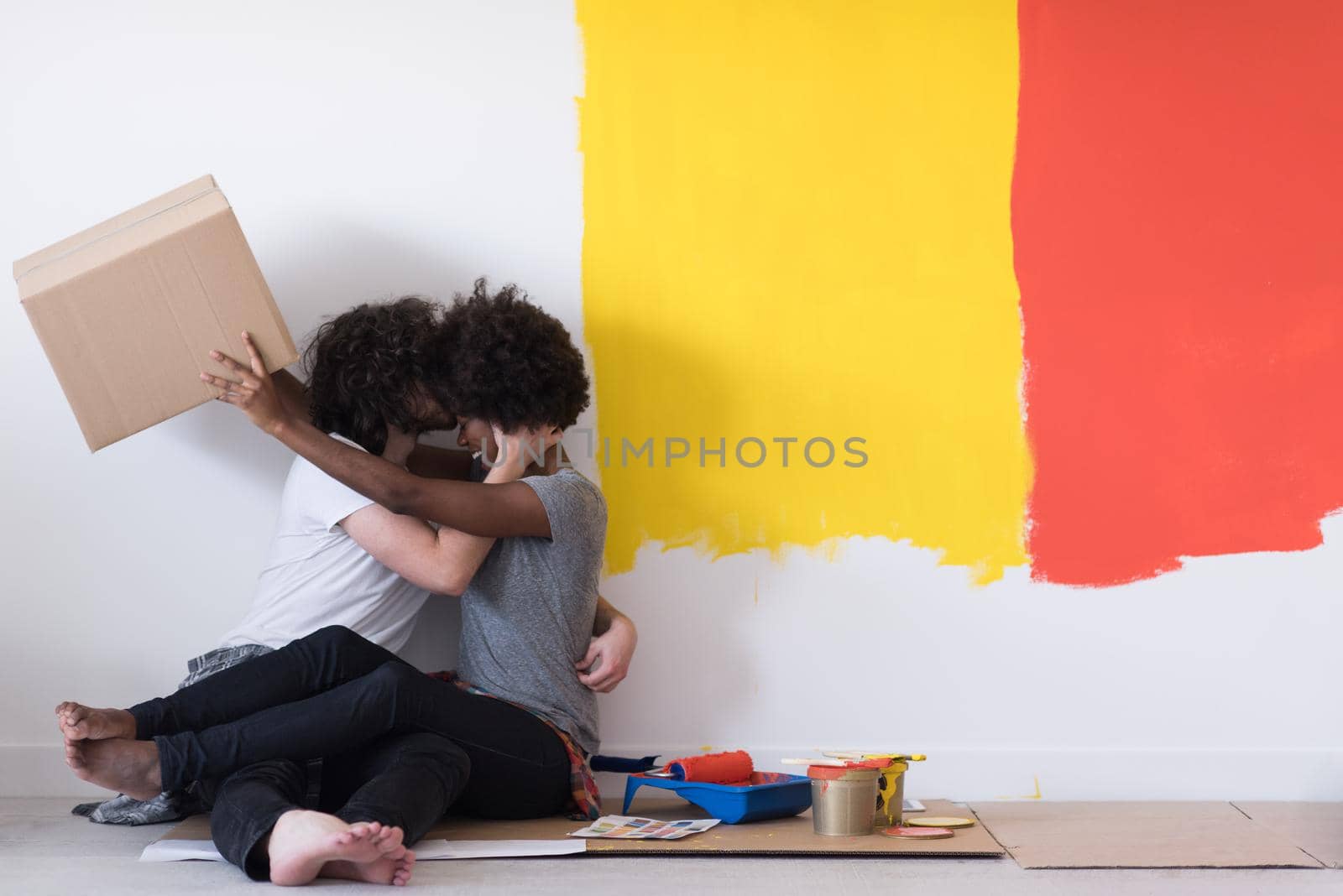 Happy young multiethnic couple relaxing and playing with cardboard boxes after painting a room in their new house on the floor