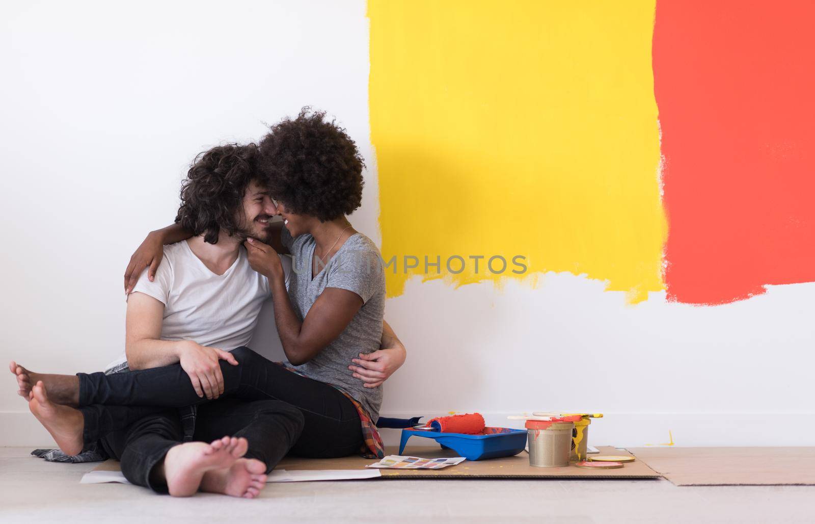 Happy young multiethnic couple relaxing after painting a room in their new house on the floor