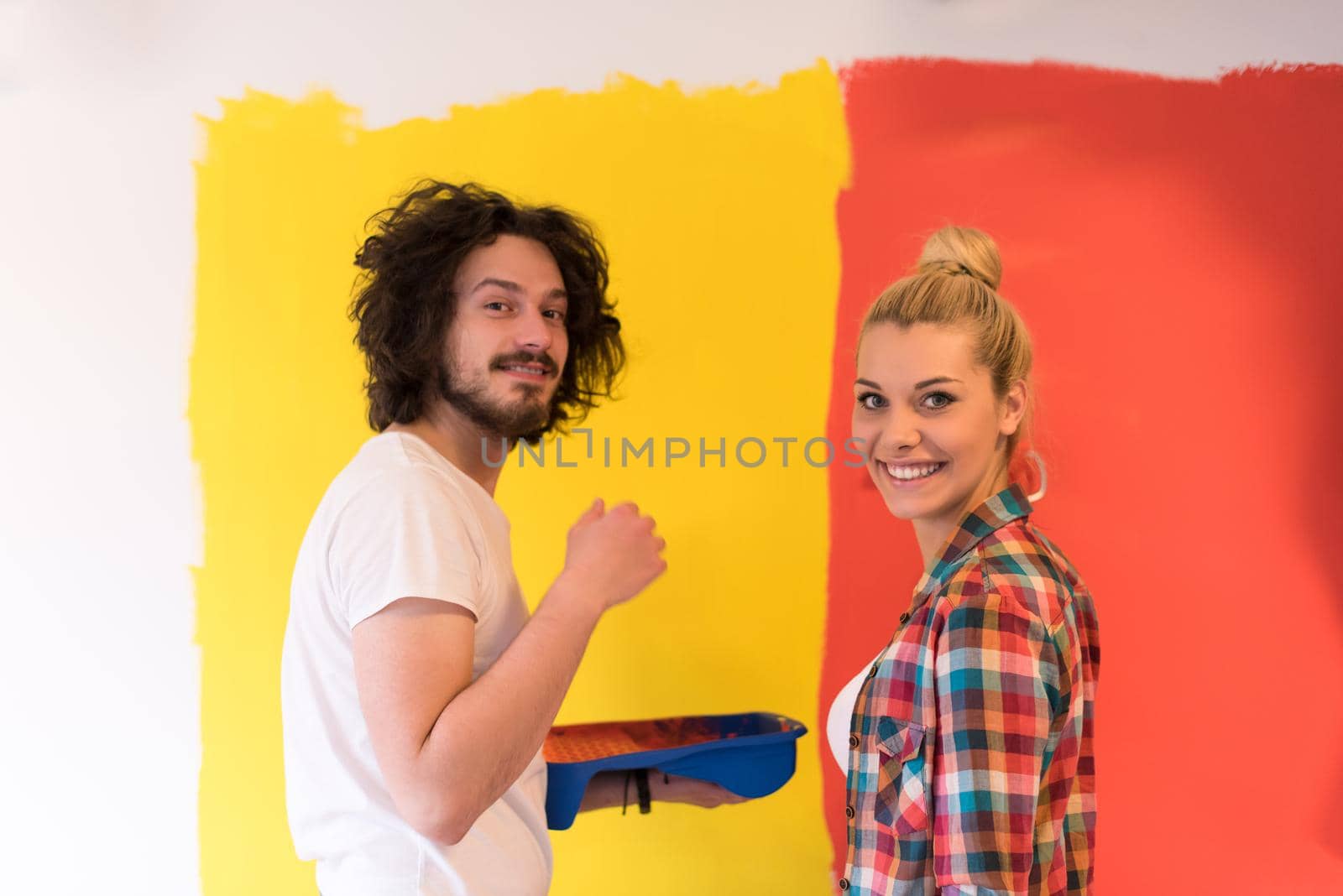 happy smiling young couple painting interior wall of new house