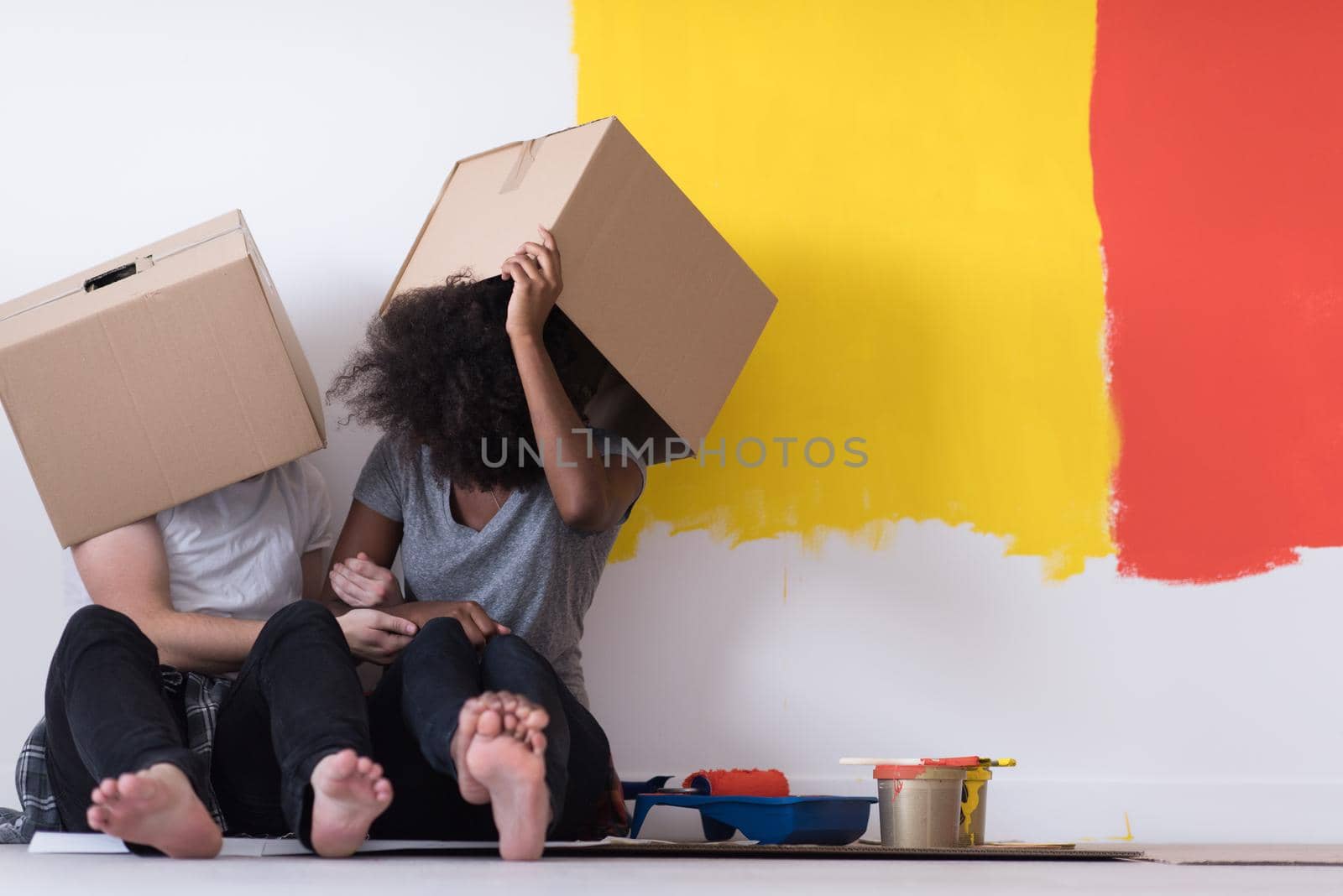 Happy young multiethnic couple relaxing and playing with cardboard boxes after painting a room in their new house on the floor