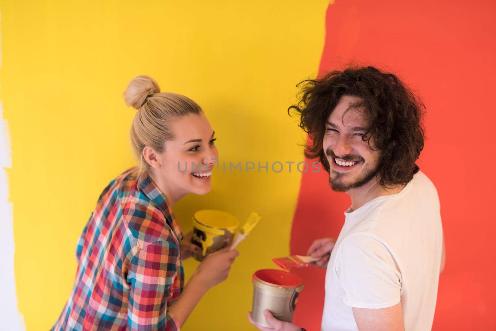 happy smiling young couple painting interior wall of new house