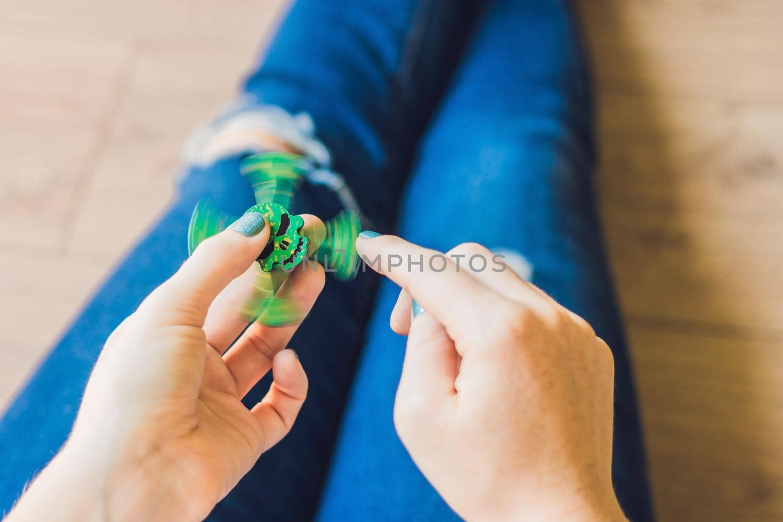 Girl teenager in holey jeans holds in hands and plays with spinner.