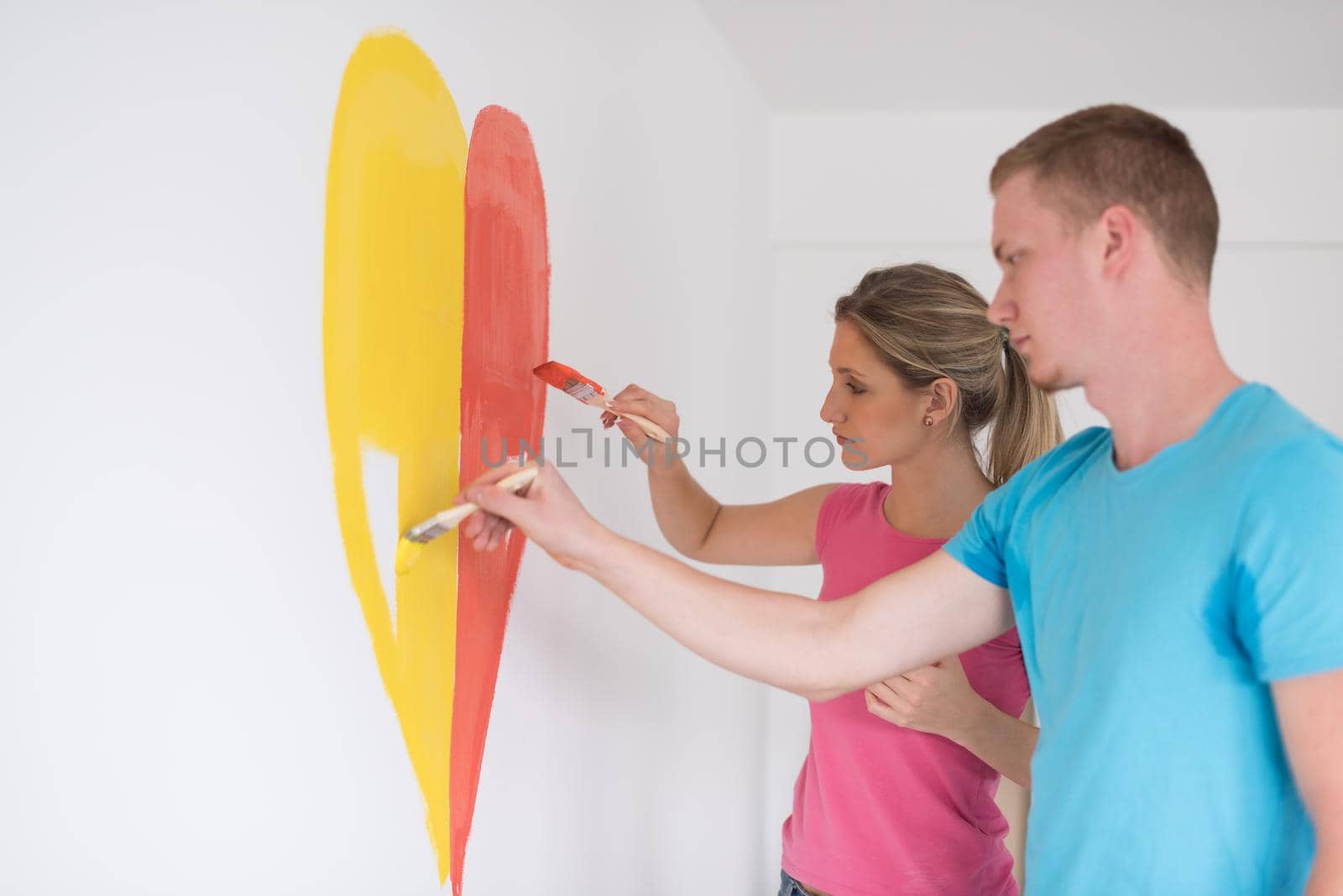 Young happy couple are painting a heart on the wall while doing repair at home.