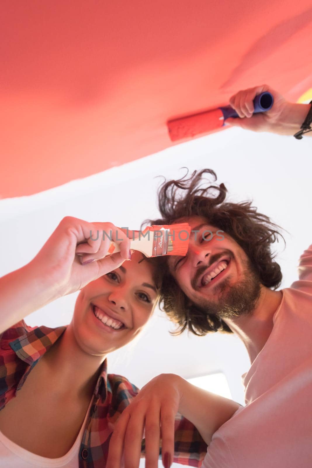 happy smiling young couple painting interior wall of new house