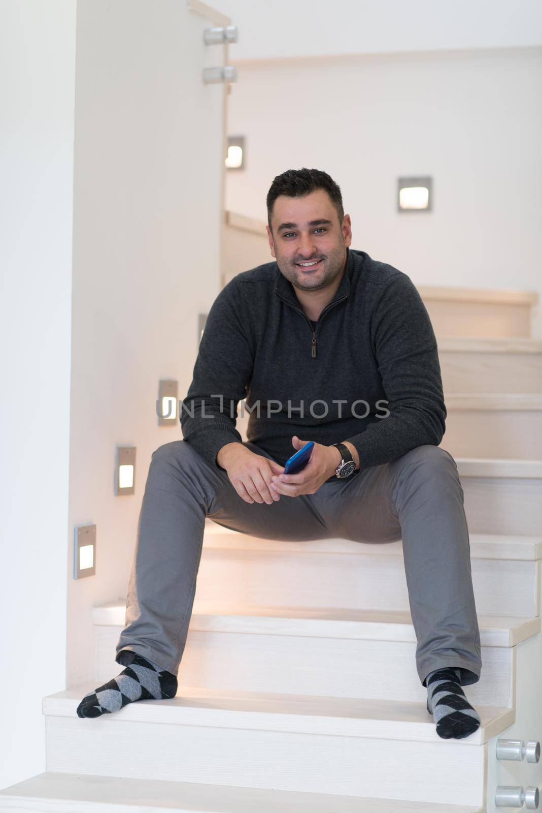 portrait of a smiling young man sitting on the stairs with a cell phone in the hands