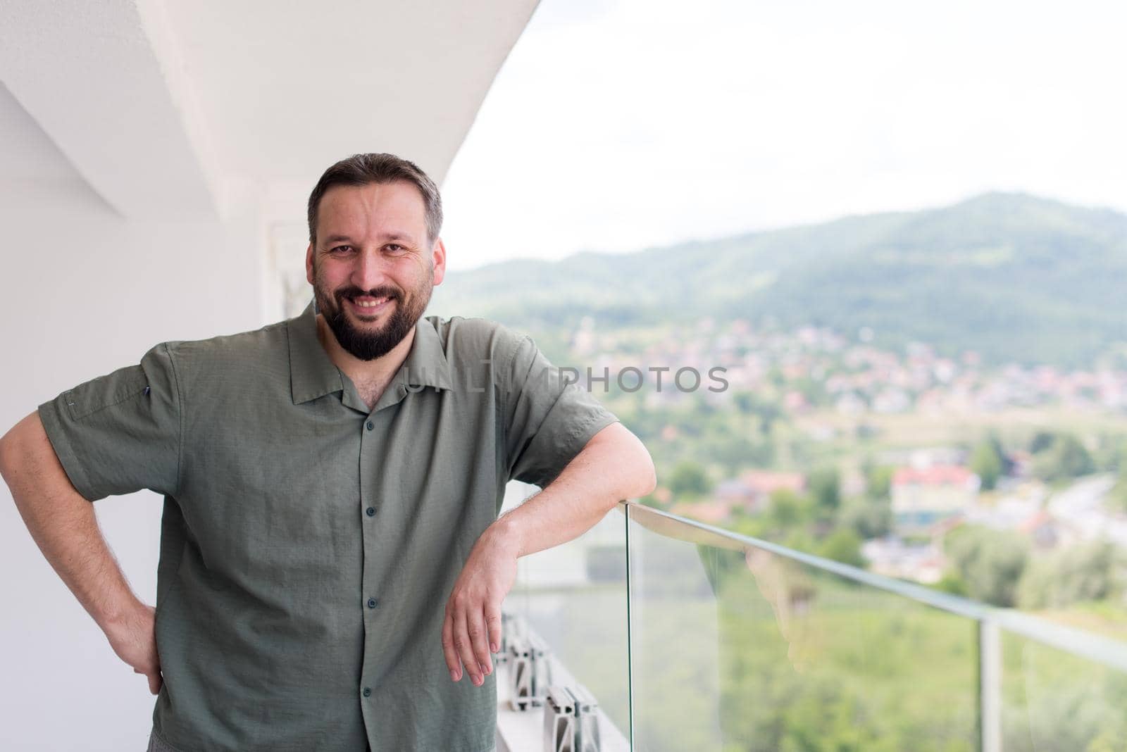 Portrait of successful happy young hipster man standing on a modern balcony overlooking the city in the background