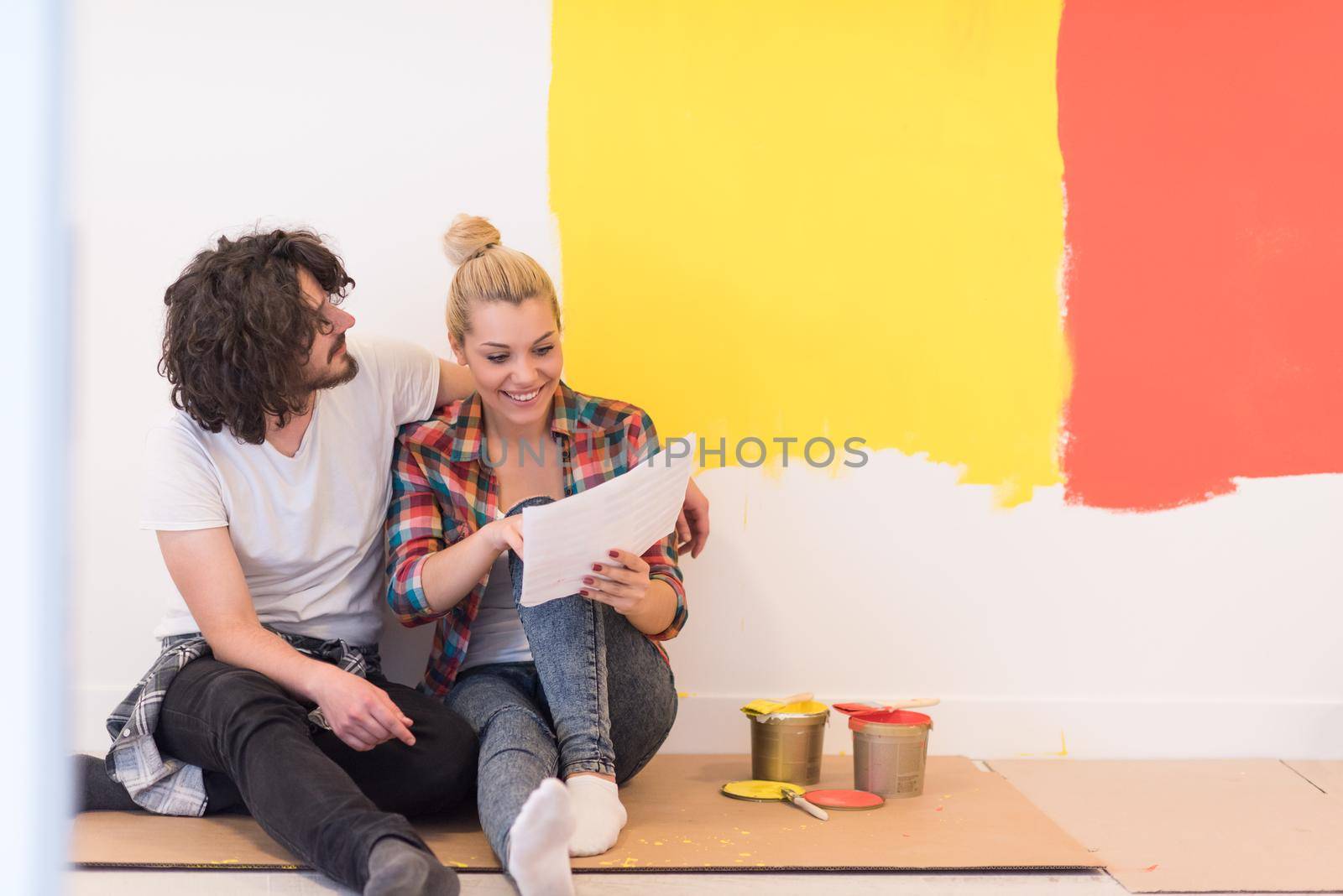 Happy young couple relaxing after painting a room in their new house on the floor
