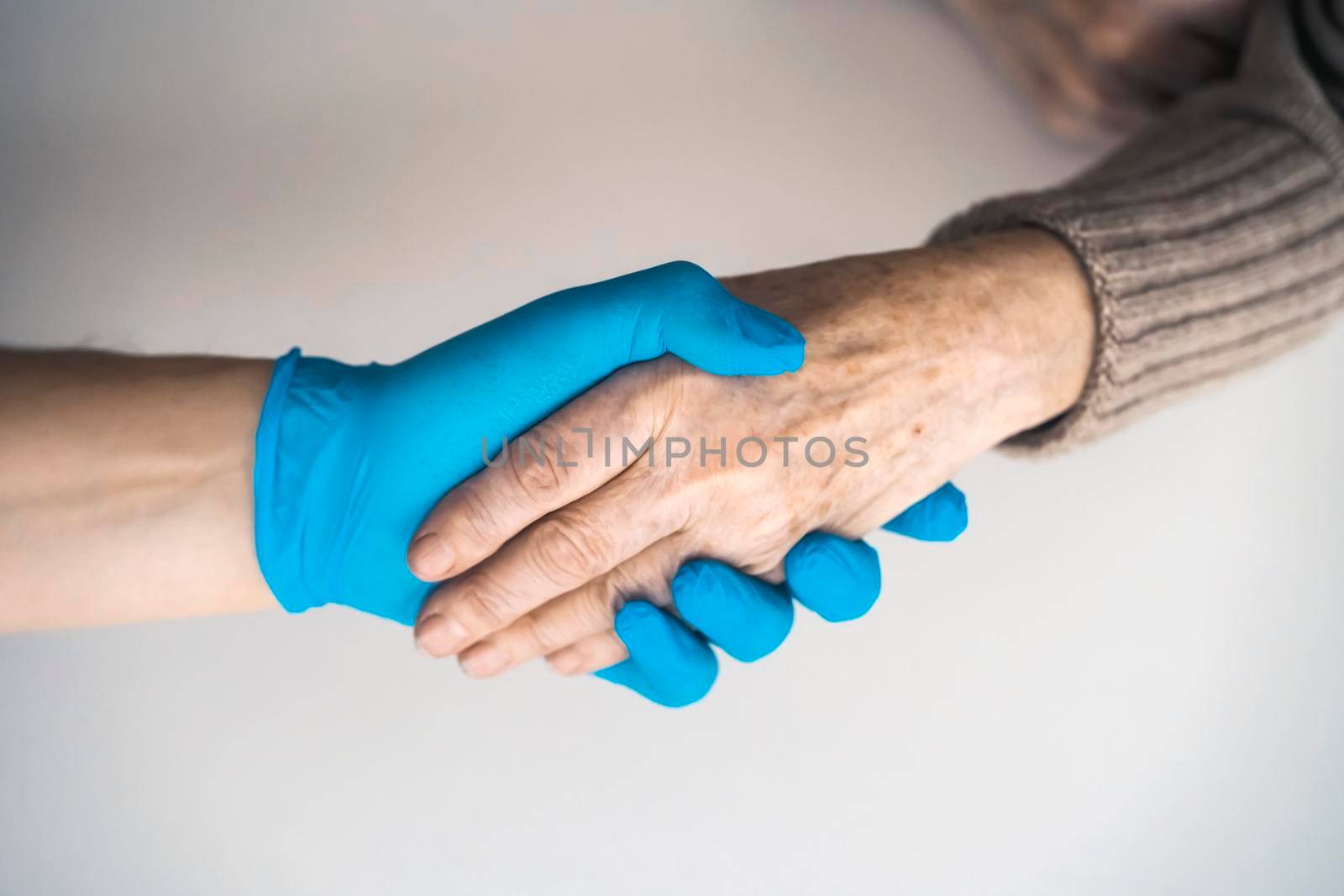 Handshake, caring, trust and support. A doctor's hand in a blue glove holds the hand of an elderly woman, a patient. Medicine and healthcare.