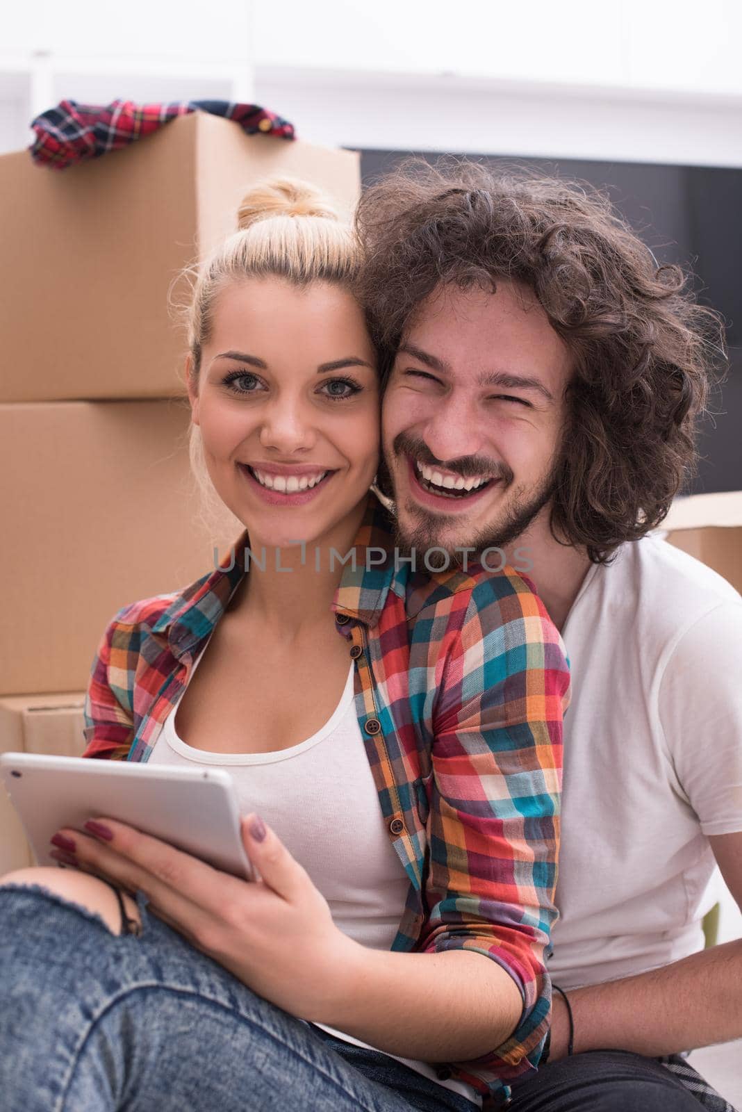 Relaxing in new house. Cheerful young couple sitting on the floor while cardboard boxes laying all around them