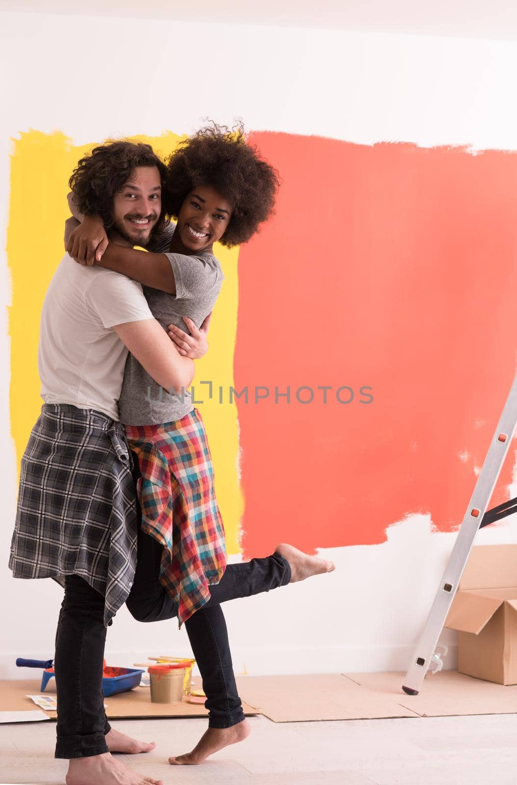 Young happy multiethnic couple hugging while they painting a wall in their new home
