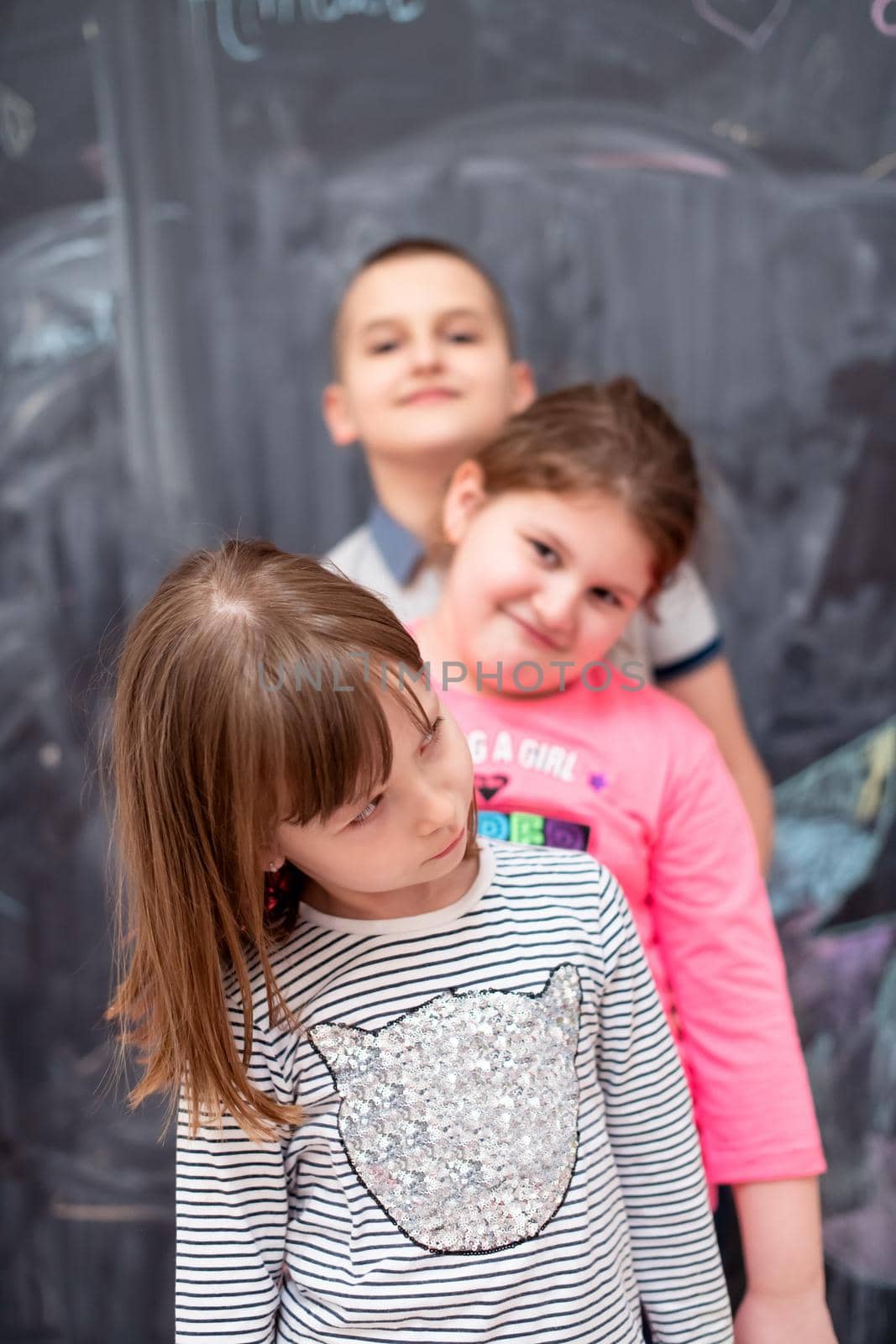 group portrait of happy childrens standing one behind the other while having fun in front of black chalkboard