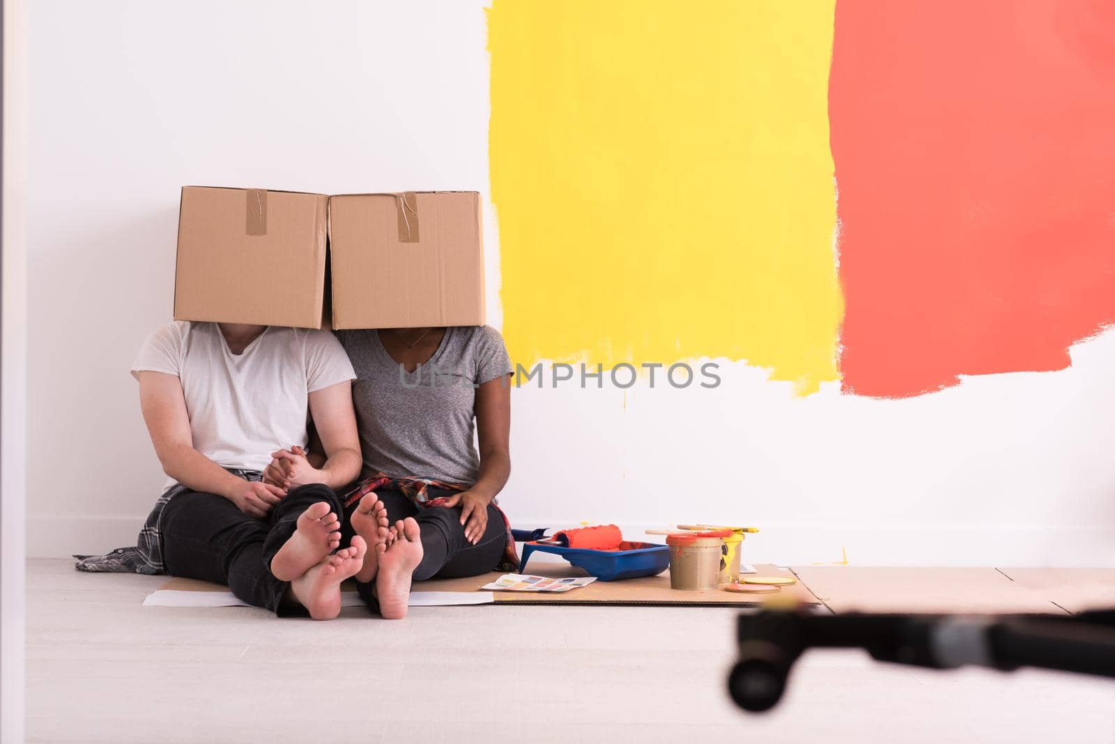 Happy young multiethnic couple relaxing and playing with cardboard boxes after painting a room in their new house on the floor