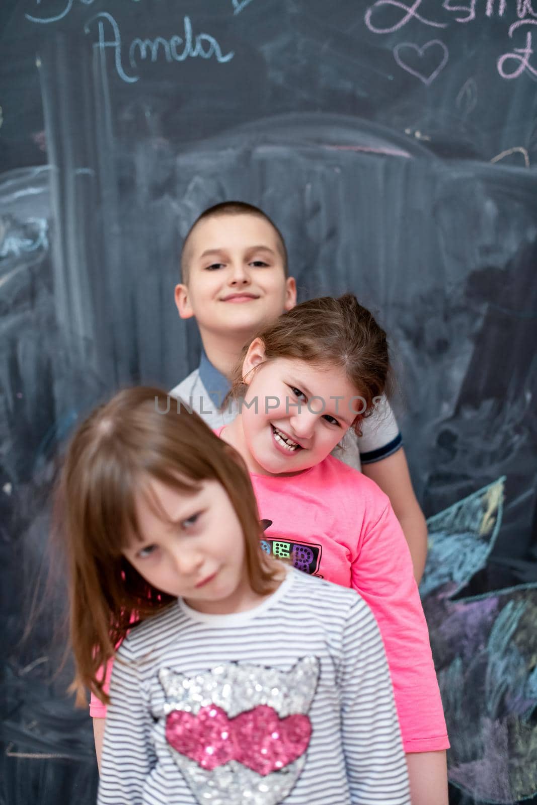 group portrait of happy childrens standing one behind the other while having fun in front of black chalkboard