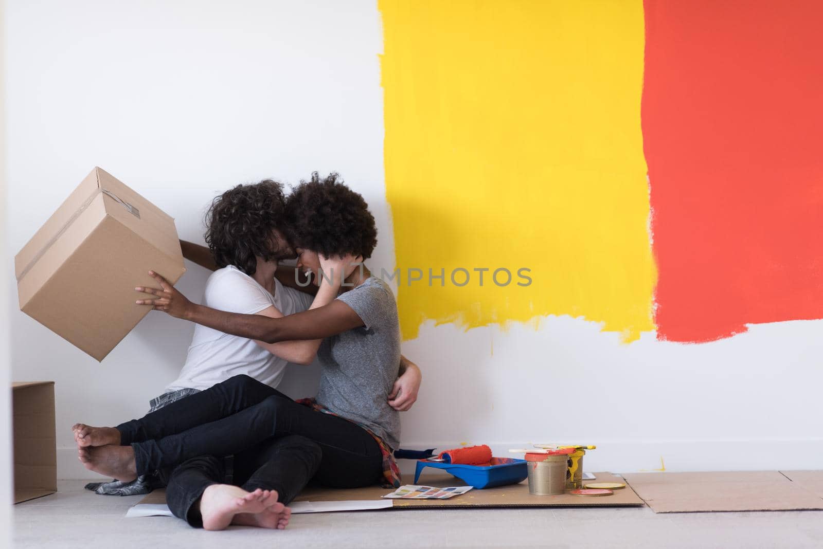 Happy young multiethnic couple relaxing and playing with cardboard boxes after painting a room in their new house on the floor