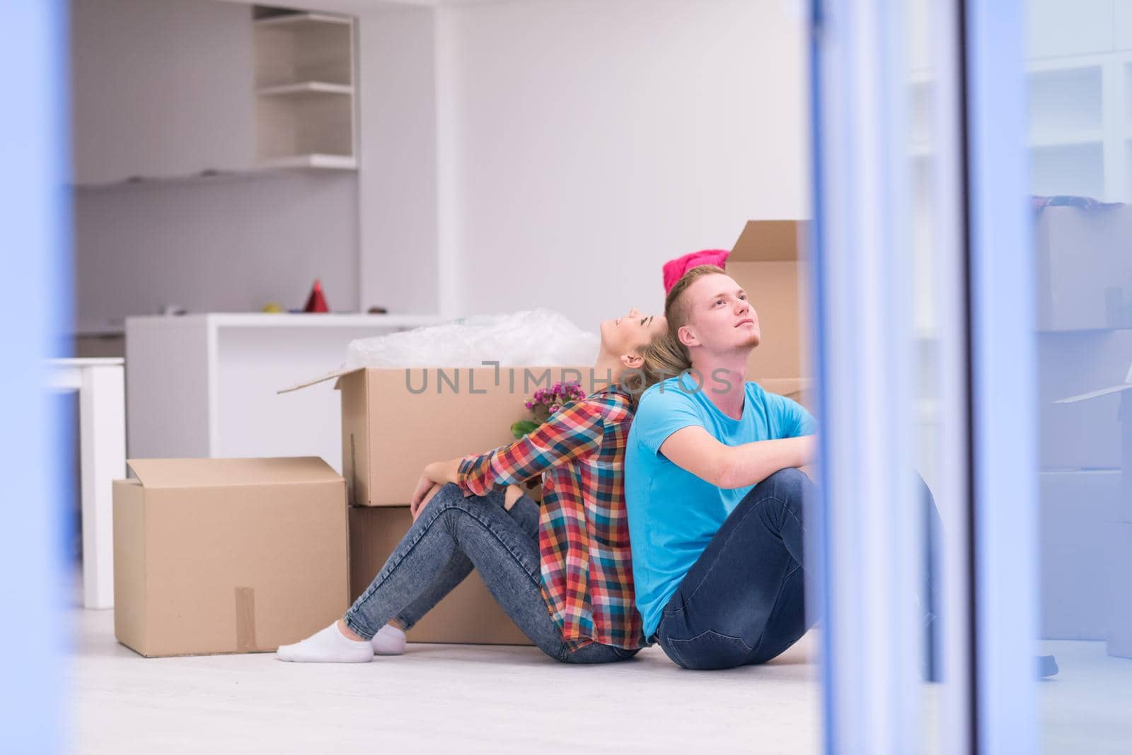 Relaxing in new house. Cheerful young couple sitting on the floor while cardboard boxes laying all around them