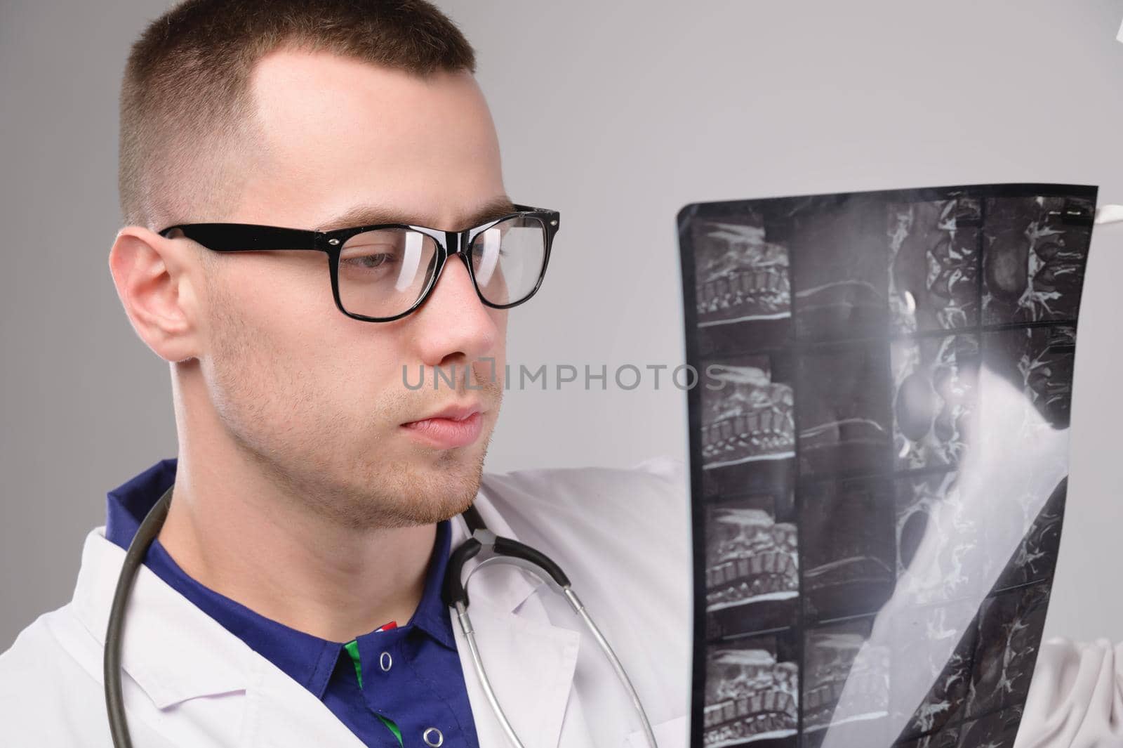 Young caucasian doctor a radiologist is looking at an x-ray. A doctor in a white coat with glasses with a stethoscope holds an x-ray in his hand.