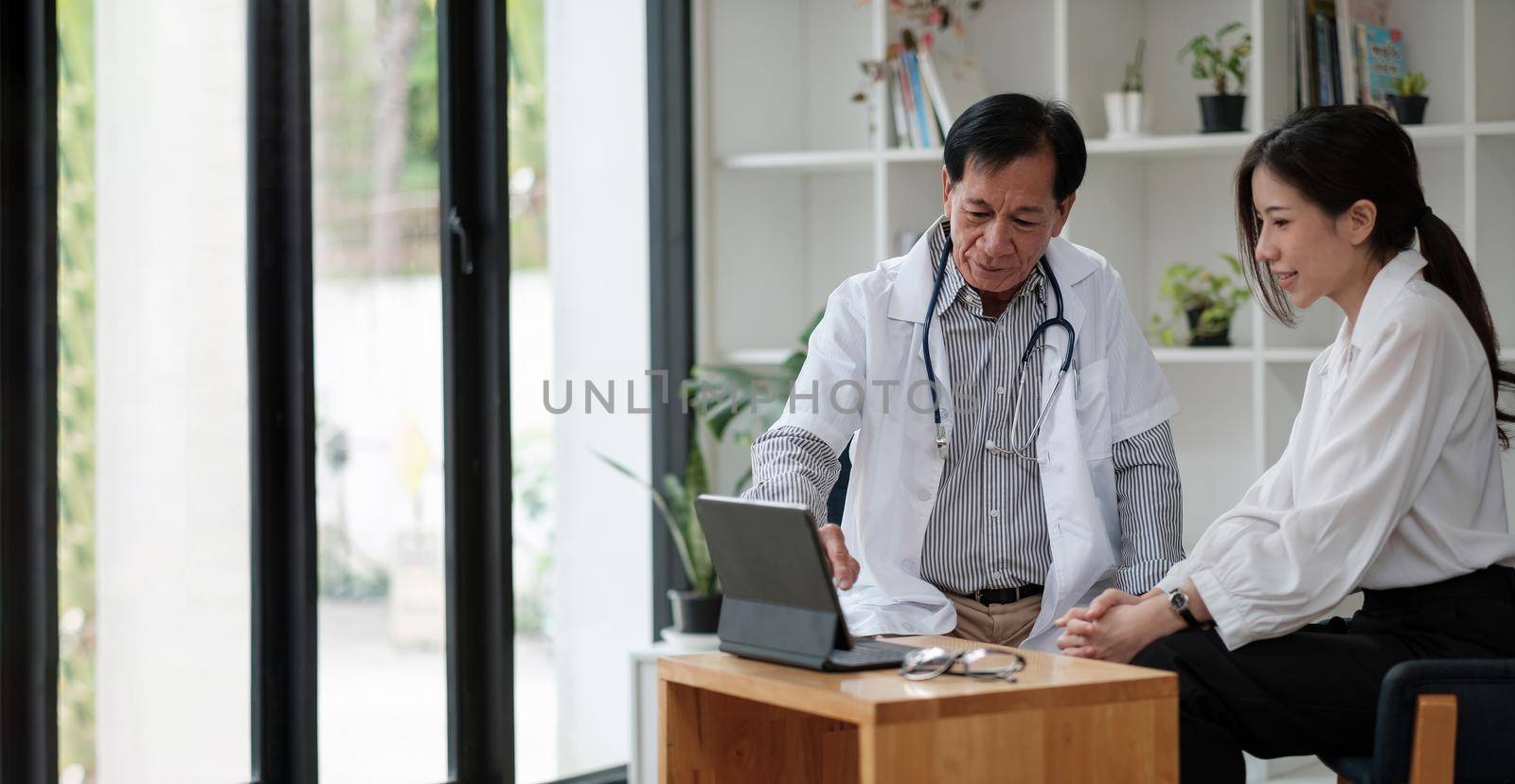Senior asian doctor physician consulting young female patient, talking to client at medical checkup visit. Geriatric diseases treatment. Elderly medical health care concept