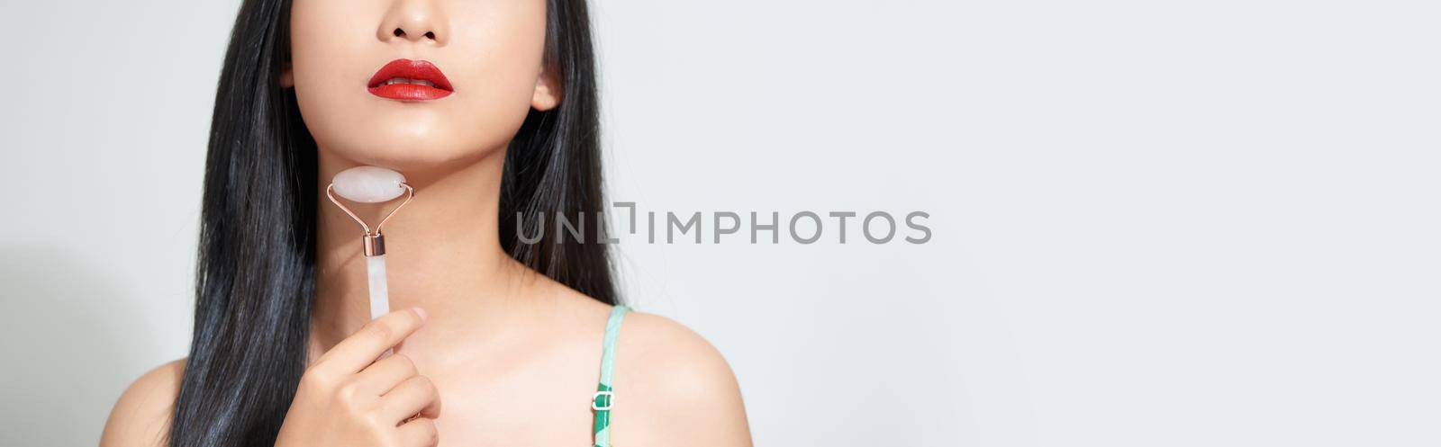 Close up photo of a young woman looking relaxed and smiling while using a natural rose quartz face roller by makidotvn