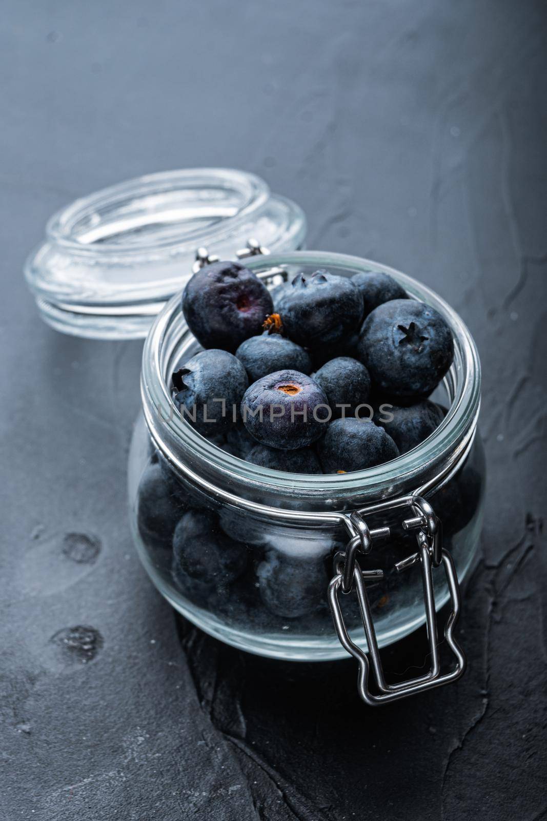 Ripe blueberry in glass jar, on black background.