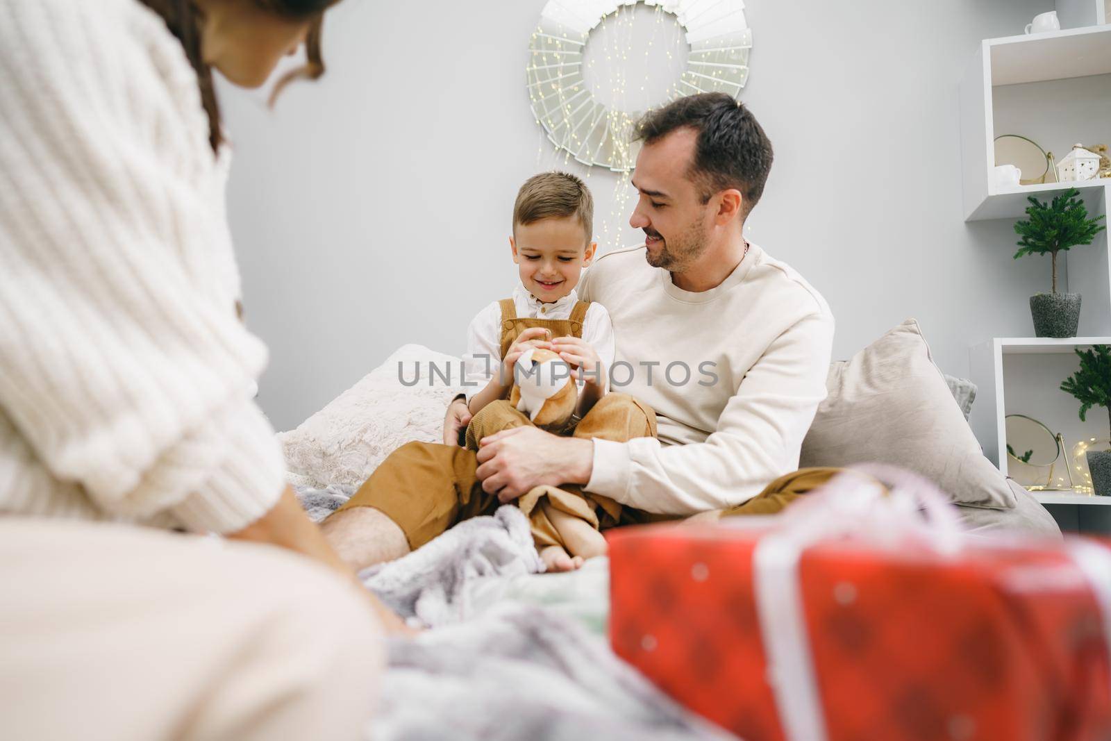 Smiling parents giving Christmas present to son at home by Fabrikasimf