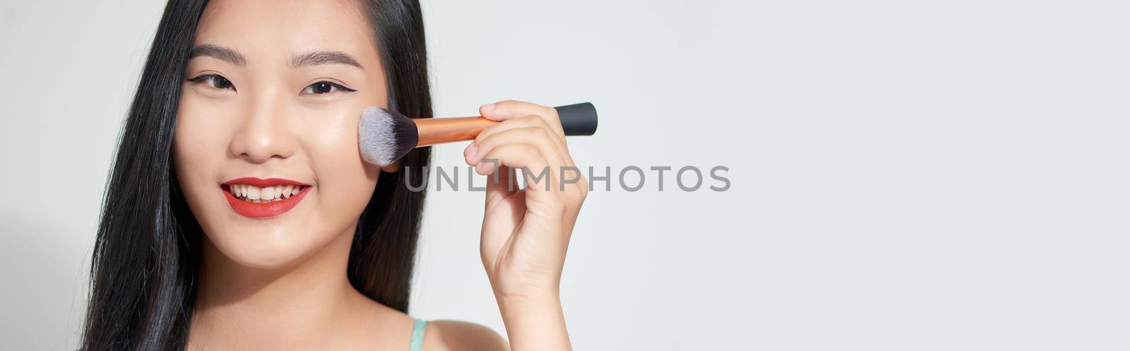 Long hair asian young beautiful woman smile and fun, touch her face and hold cosmetic powder brush set on white