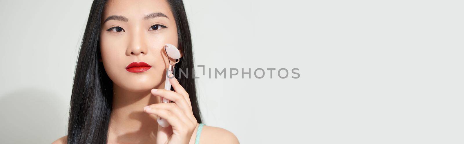 Face massage. Smiling woman using rose quartz facial roller for skin care, beauty treatment on white isolate background.