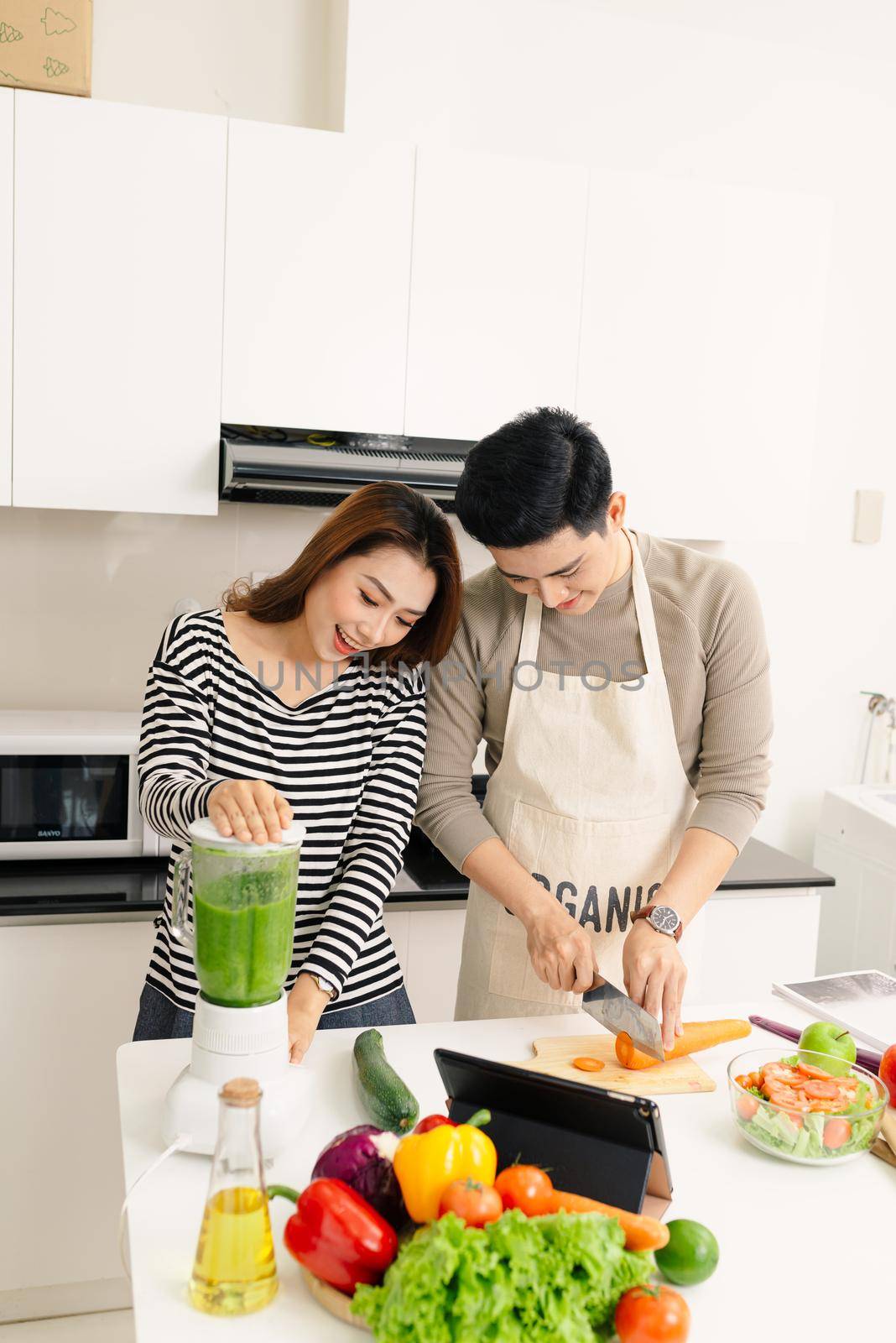 happy young couple have fun in modern kitchen indoor while preparing fresh fruits and vegetables food salad by makidotvn