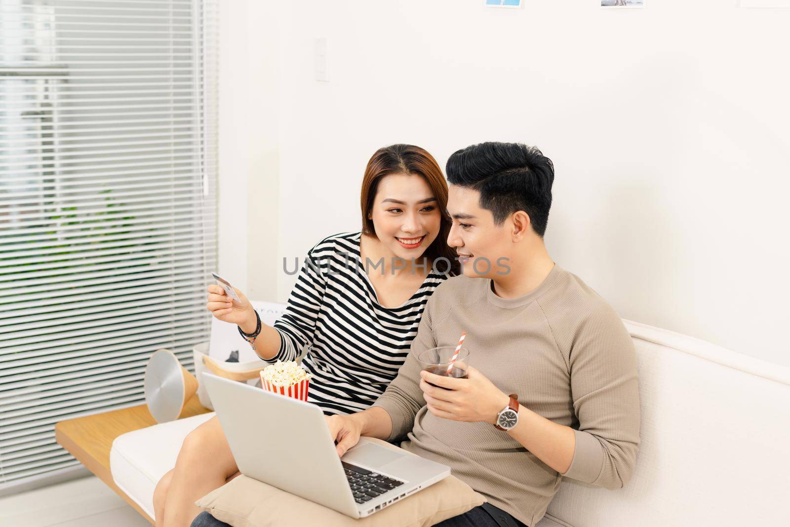 Portrait of young asian couple relaxing and watching a movie with laptop on couch at home.