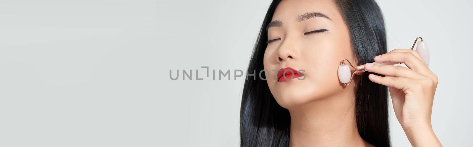 Face massage. Smiling woman using rose quartz facial roller for skin care, beauty treatment on white isolate background.