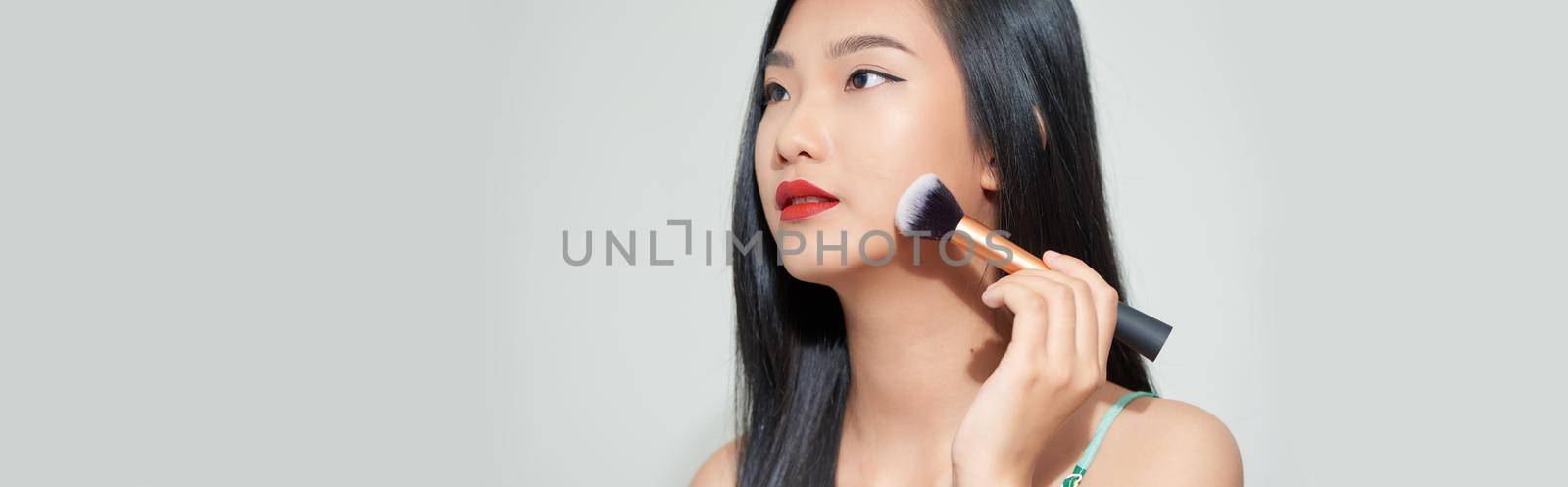 portrait of beautiful asian woman smiling while applying blush on isolated on white background