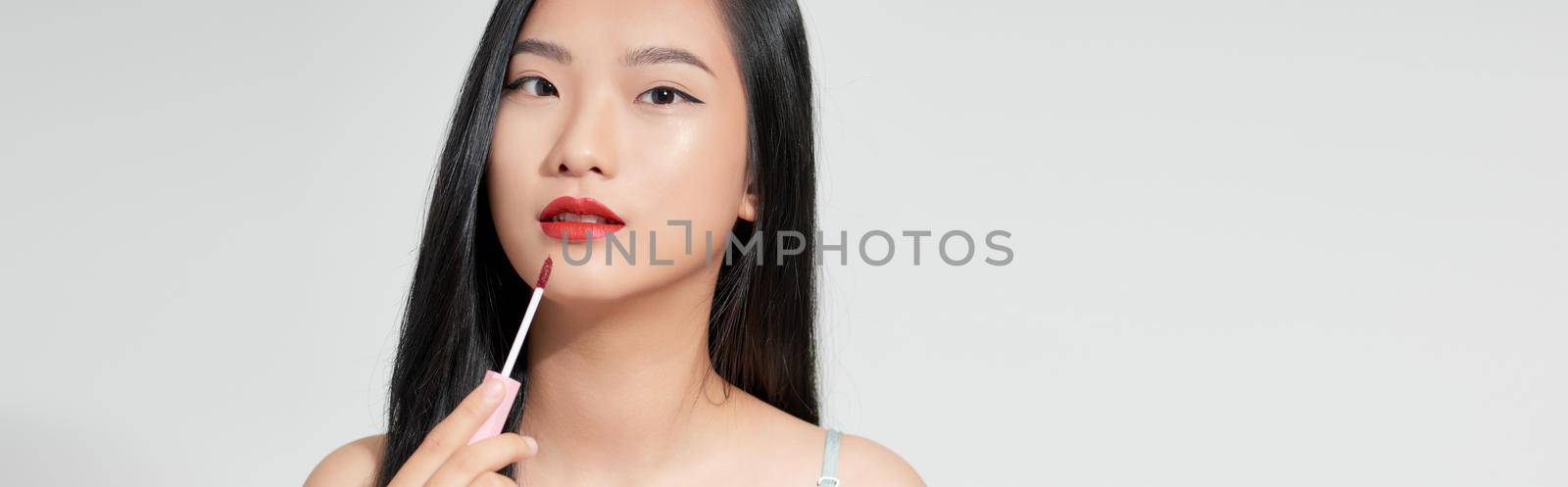 Attractive and beautiful Asian girl paint lips a pink lipstick, smiling make-up girl isolated on white background