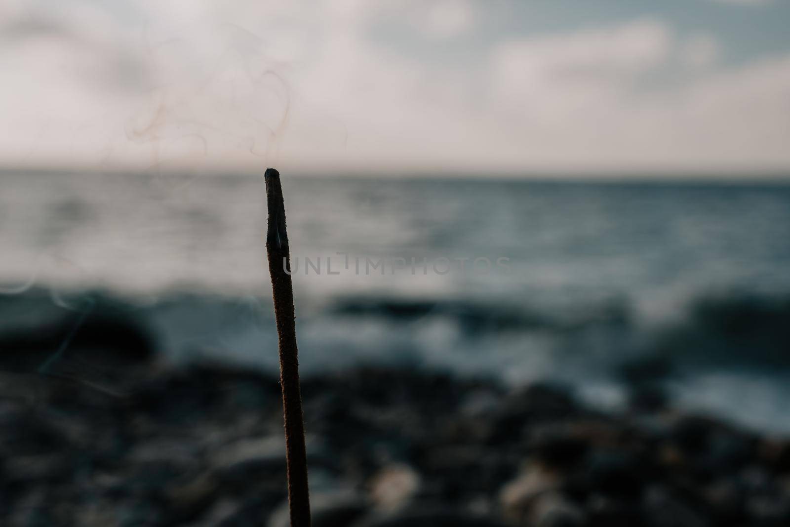 Close up of incense aroma stick burning on the sea shore. Meditation concept. Morning sea waves washing plate with aroma stick.
