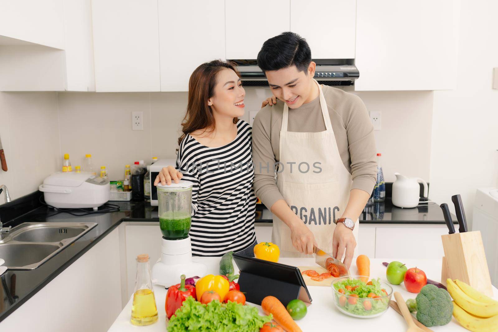 Laughing asian couple preparing healthy food together in light kitchen