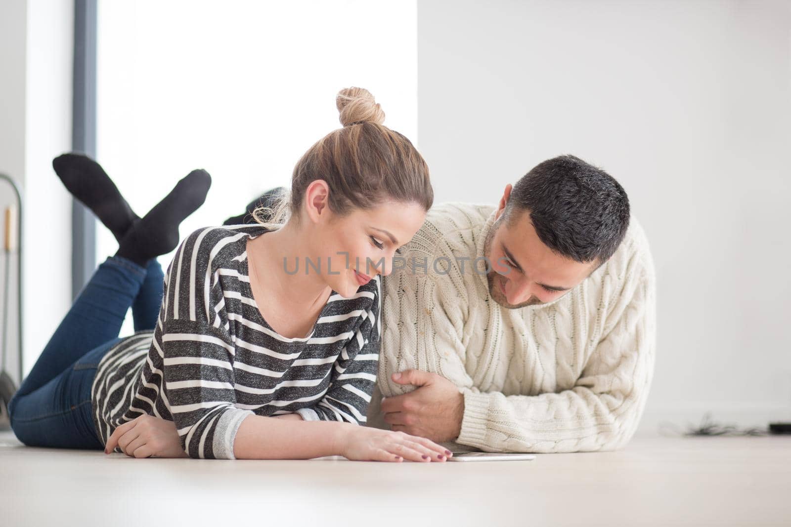 Young Couple on the floor in front of fireplace surfing internet using digital tablet on cold winter day