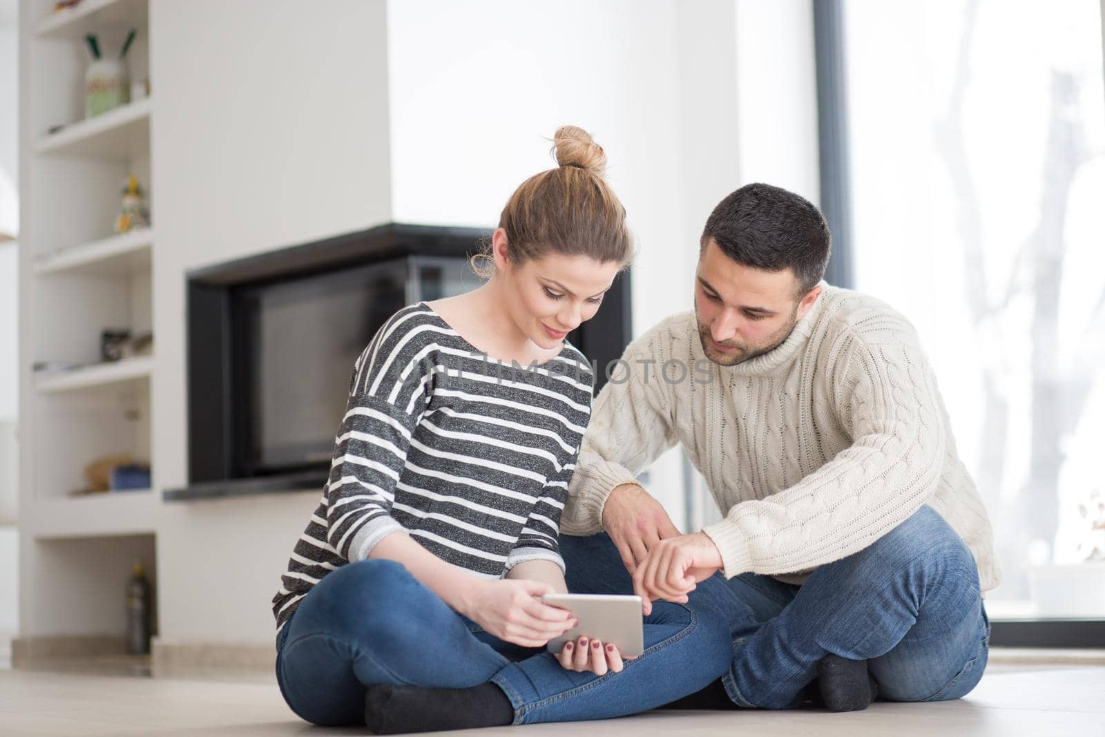 Young Couple on the floor in front of fireplace surfing internet using digital tablet on cold winter day