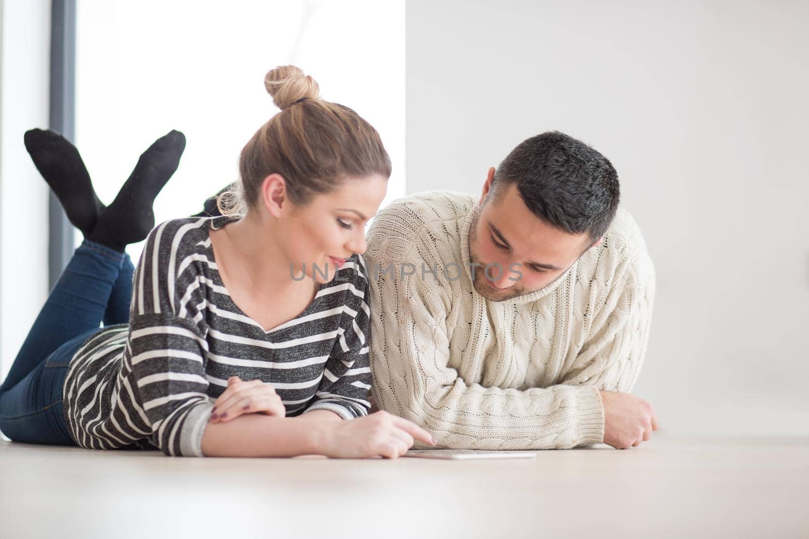 Young Couple on the floor in front of fireplace surfing internet using digital tablet on cold winter day