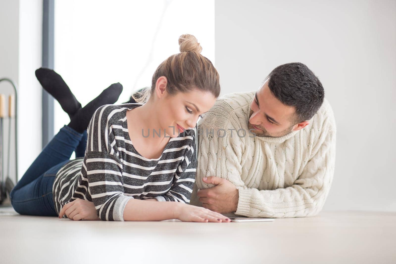 Young Couple on the floor in front of fireplace surfing internet using digital tablet on cold winter day