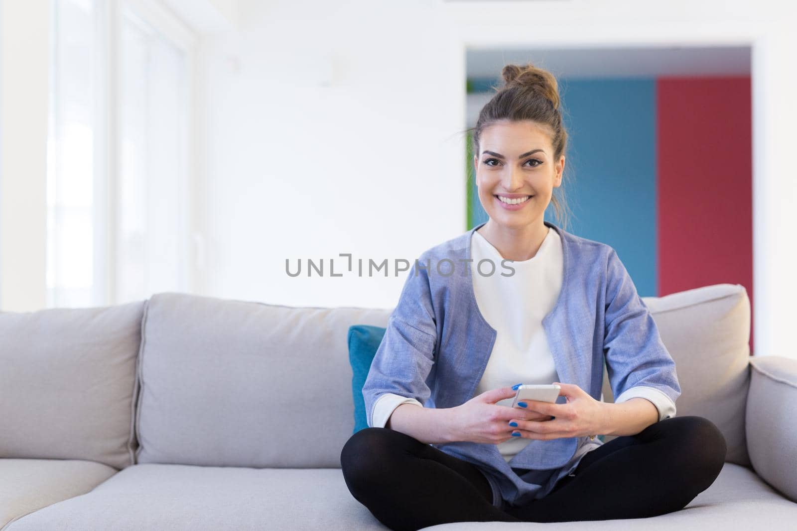 young happy woman using mobile phone on sofa at luxury home