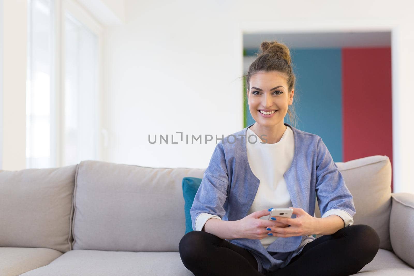 young happy woman using mobile phone on sofa at luxury home