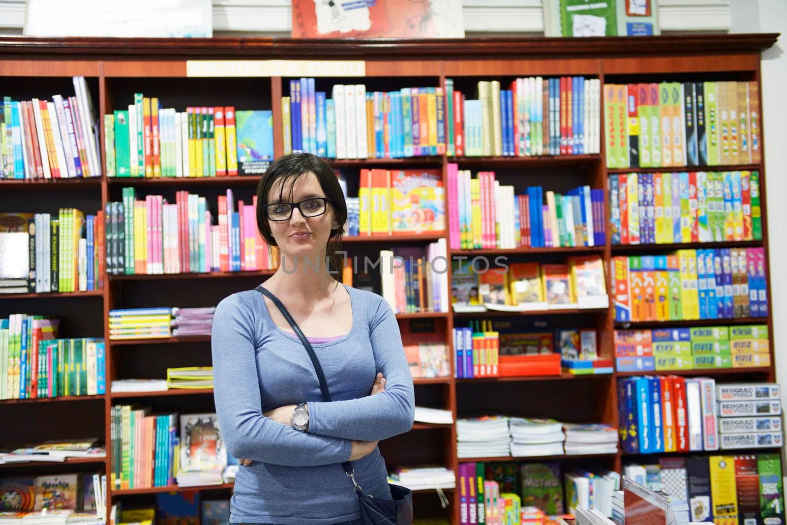Pretty female student standing at bookshelf in university library store shop  searching for a book