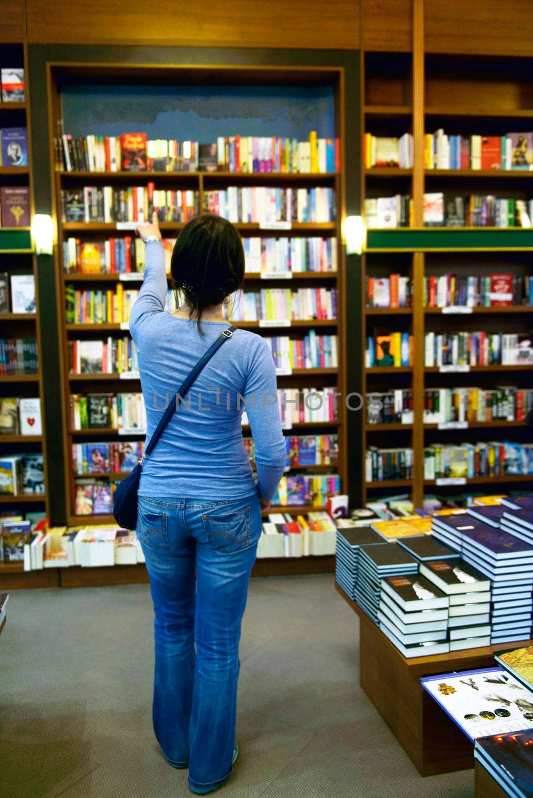 Pretty female student standing at bookshelf in university library store shop  searching for a book