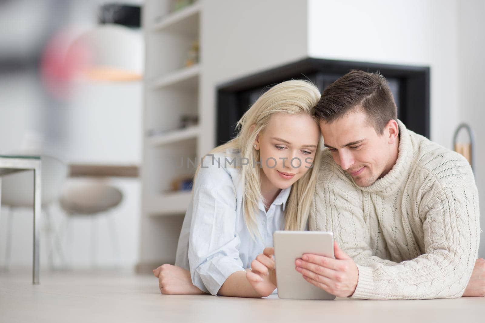 Young Couple on the floor in front of fireplace surfing internet using digital tablet on cold winter day