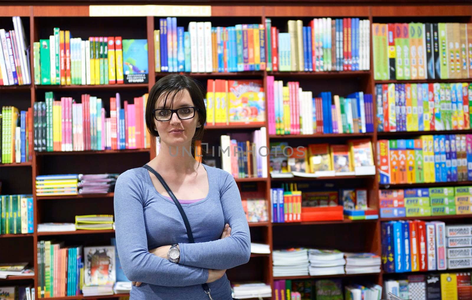 Pretty female student standing at bookshelf in university library store shop  searching for a book