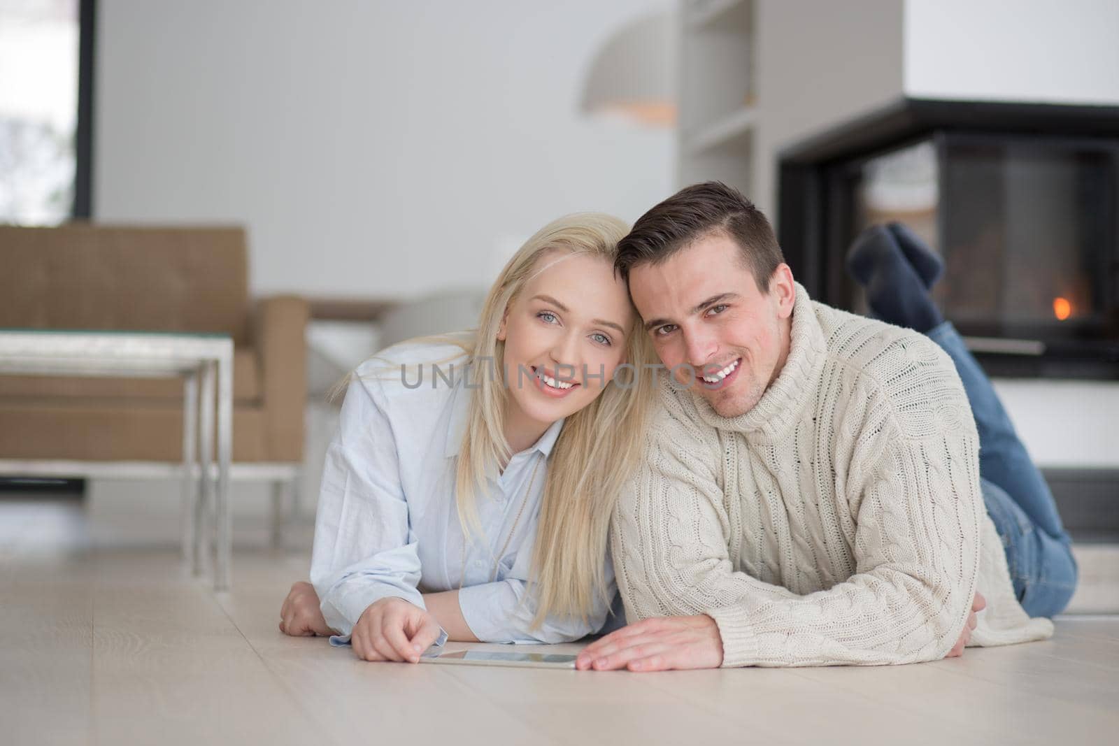 Young Couple on the floor in front of fireplace surfing internet using digital tablet on cold winter day