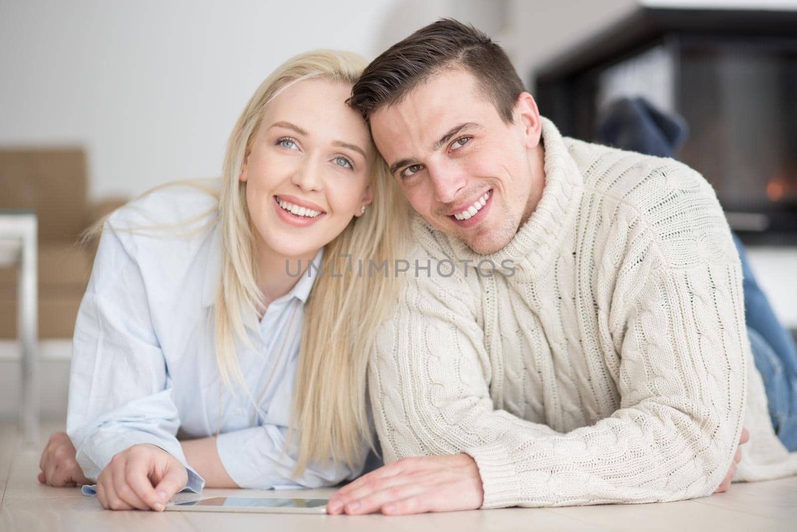 Young Couple on the floor in front of fireplace surfing internet using digital tablet on cold winter day