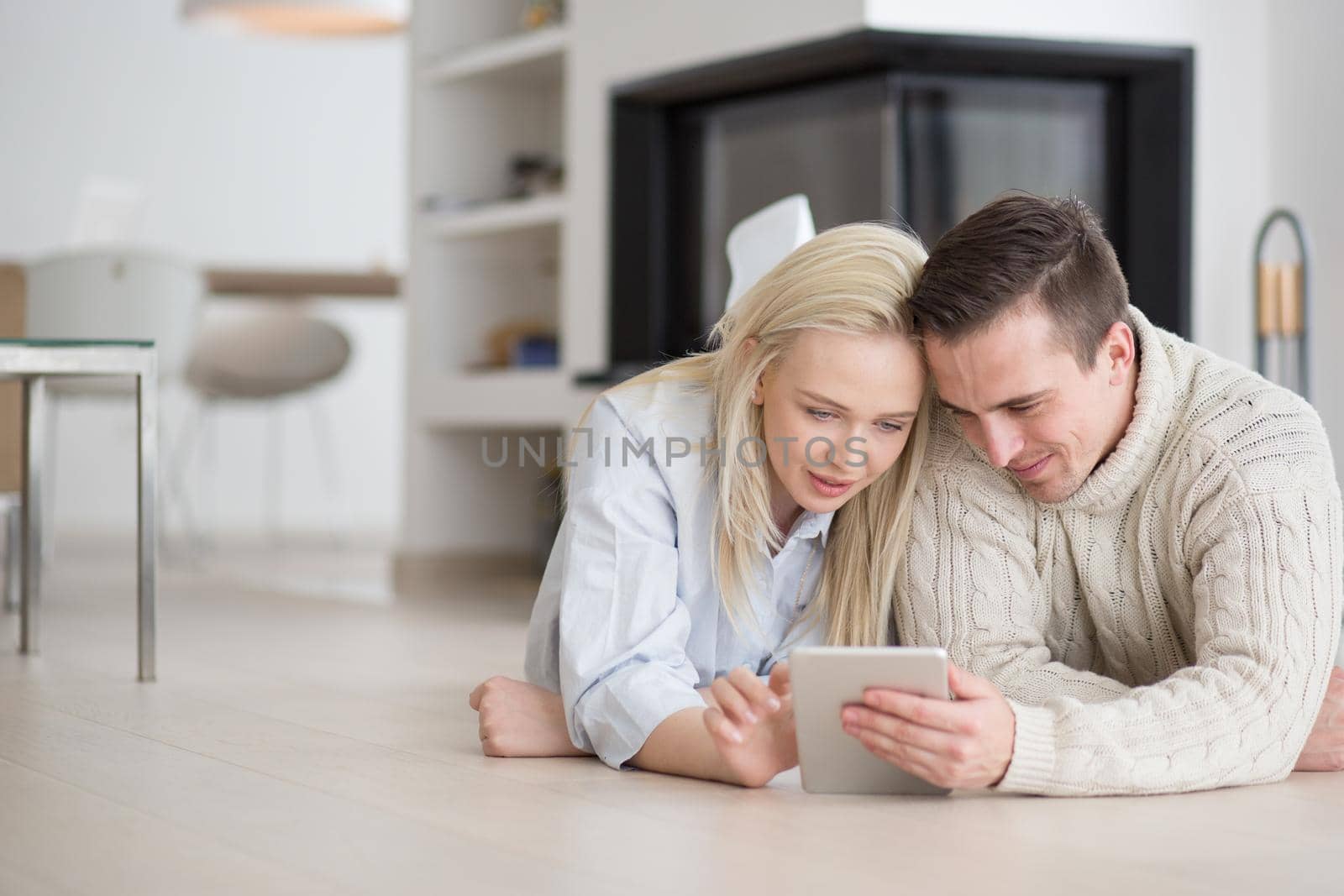 Young Couple on the floor in front of fireplace surfing internet using digital tablet on cold winter day