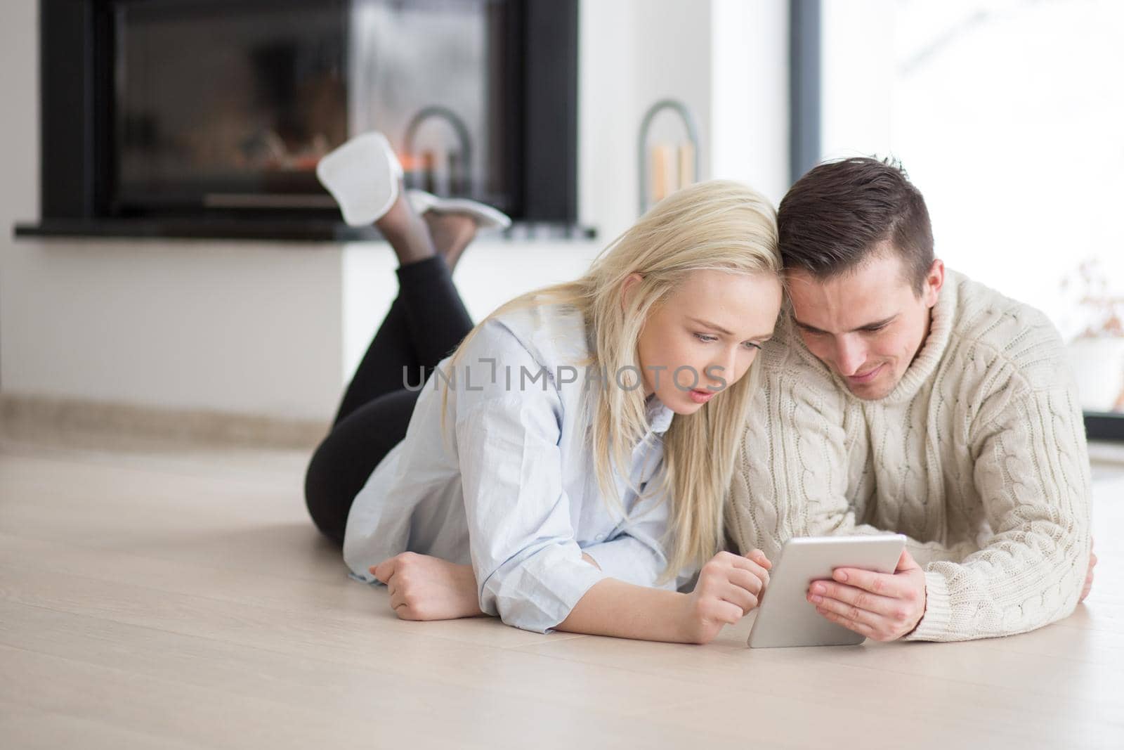 Young Couple on the floor in front of fireplace surfing internet using digital tablet on cold winter day