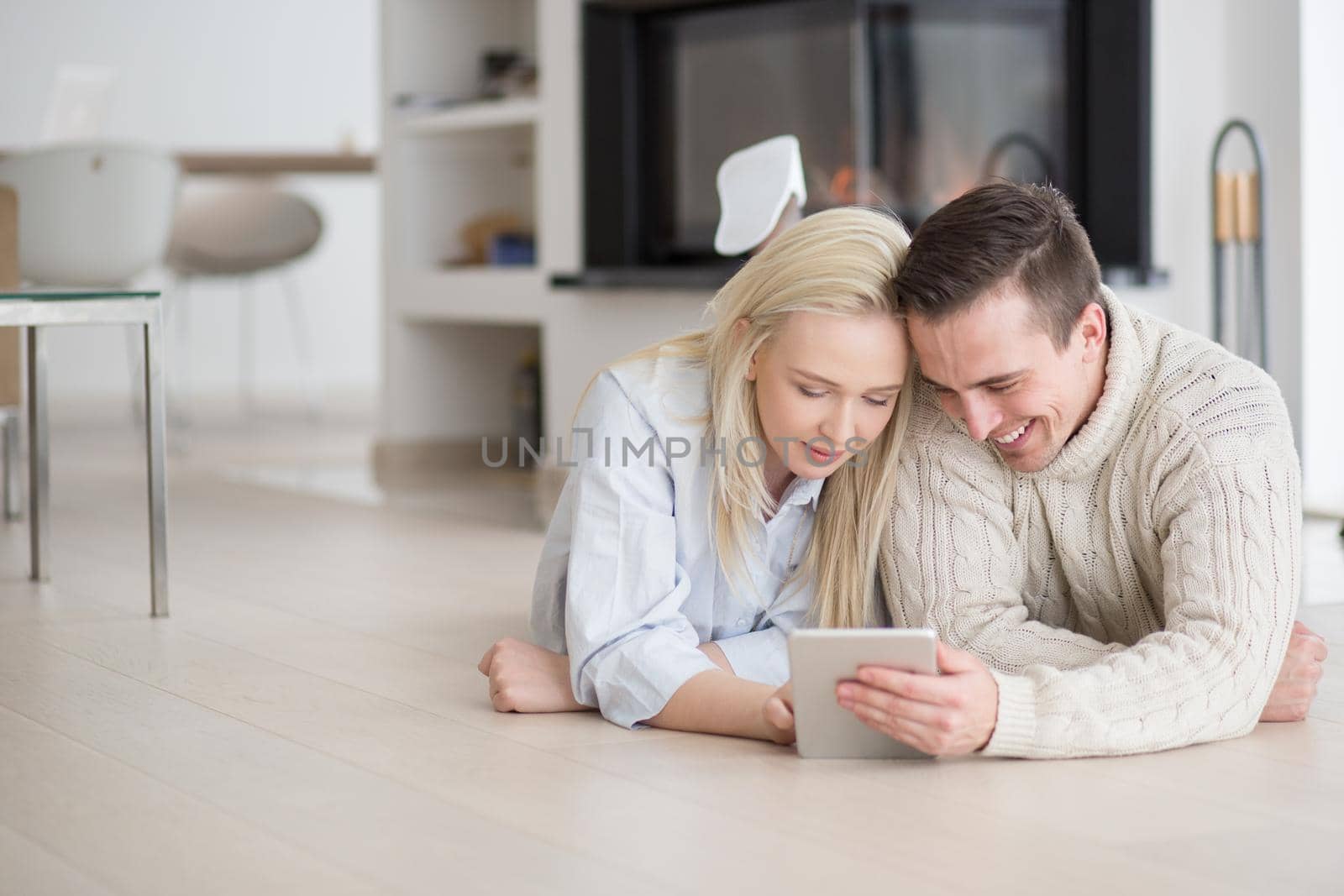 Young Couple on the floor in front of fireplace surfing internet using digital tablet on cold winter day