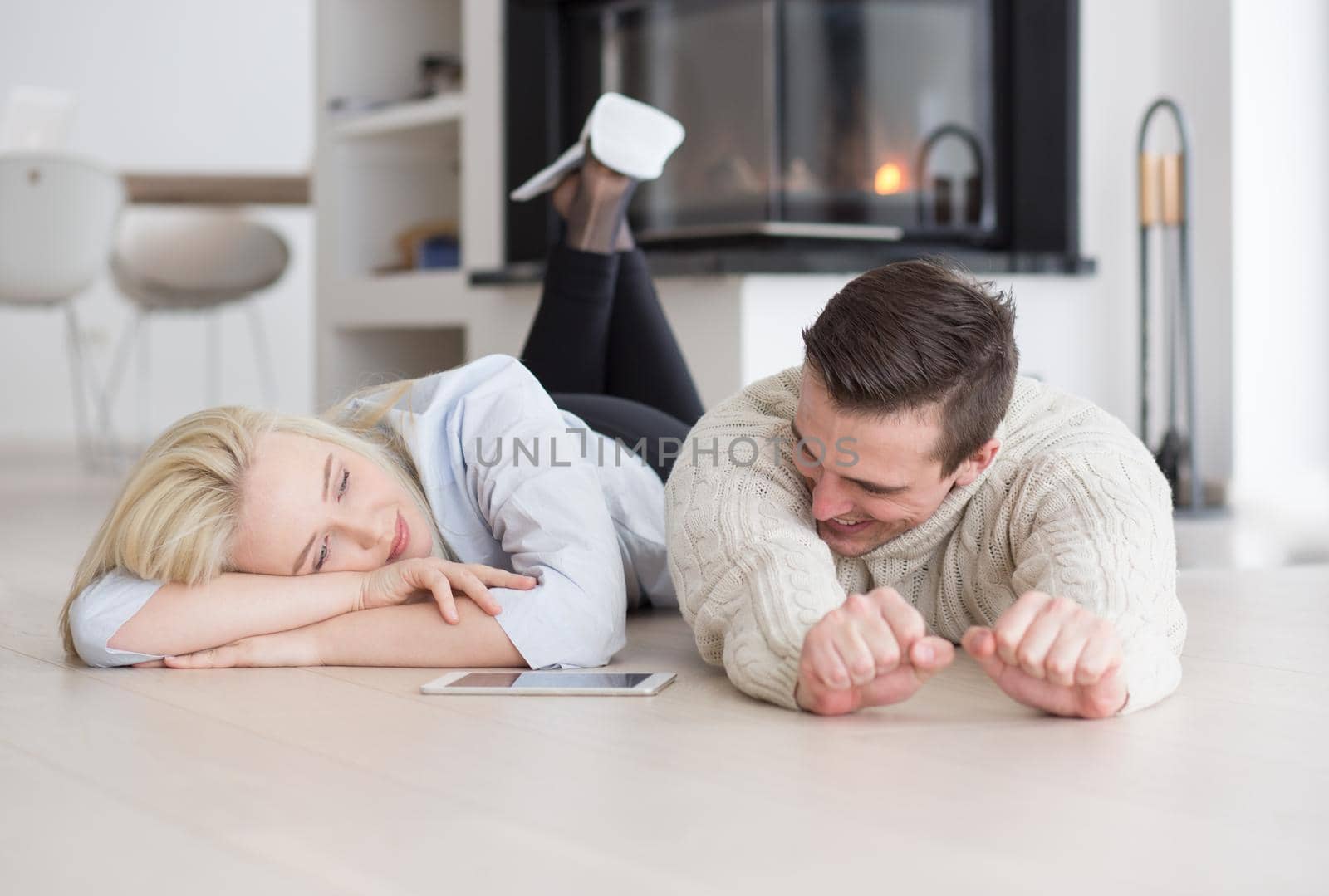 Young Couple on the floor in front of fireplace surfing internet using digital tablet on cold winter day